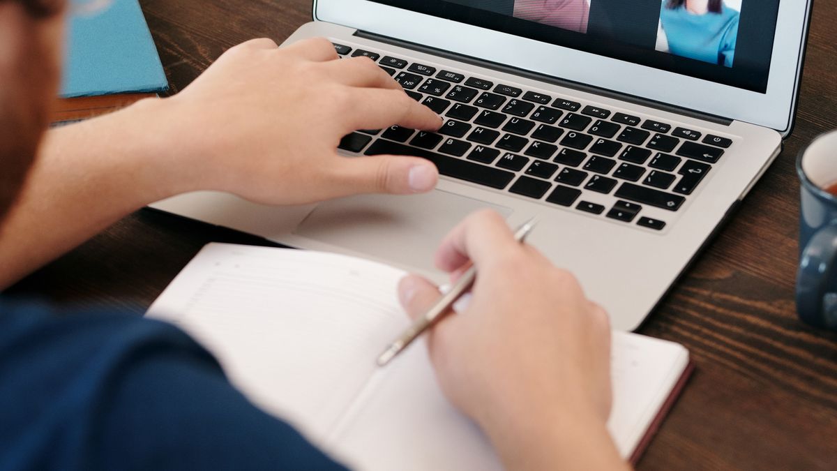 ノートPCでオンライン会議を見ながらノートにメモを取る様子